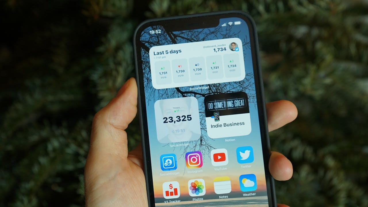A hand holding a smartphone displaying various home screen widgets and app icons.